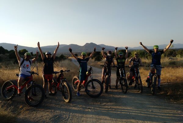 Grupo de amigos saltando de alegría junto a sus bicicletas eléctricas con el paisaje de la Sierra Oeste de Madrid de fondo